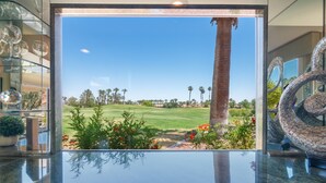 Vista desde una habitación con pared de vidrio, mostrando un campo de golf, palmeras y una escultura de vidrio decorativa.