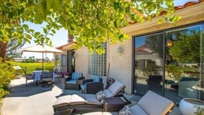 Un patio exterior con sillones de descanso, una mesa y un ventanal de vidrio que da a un área techada.