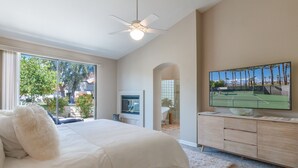 Un dormitorio con una cama grande, un ventilador de techo, un televisor y vistas al exterior.