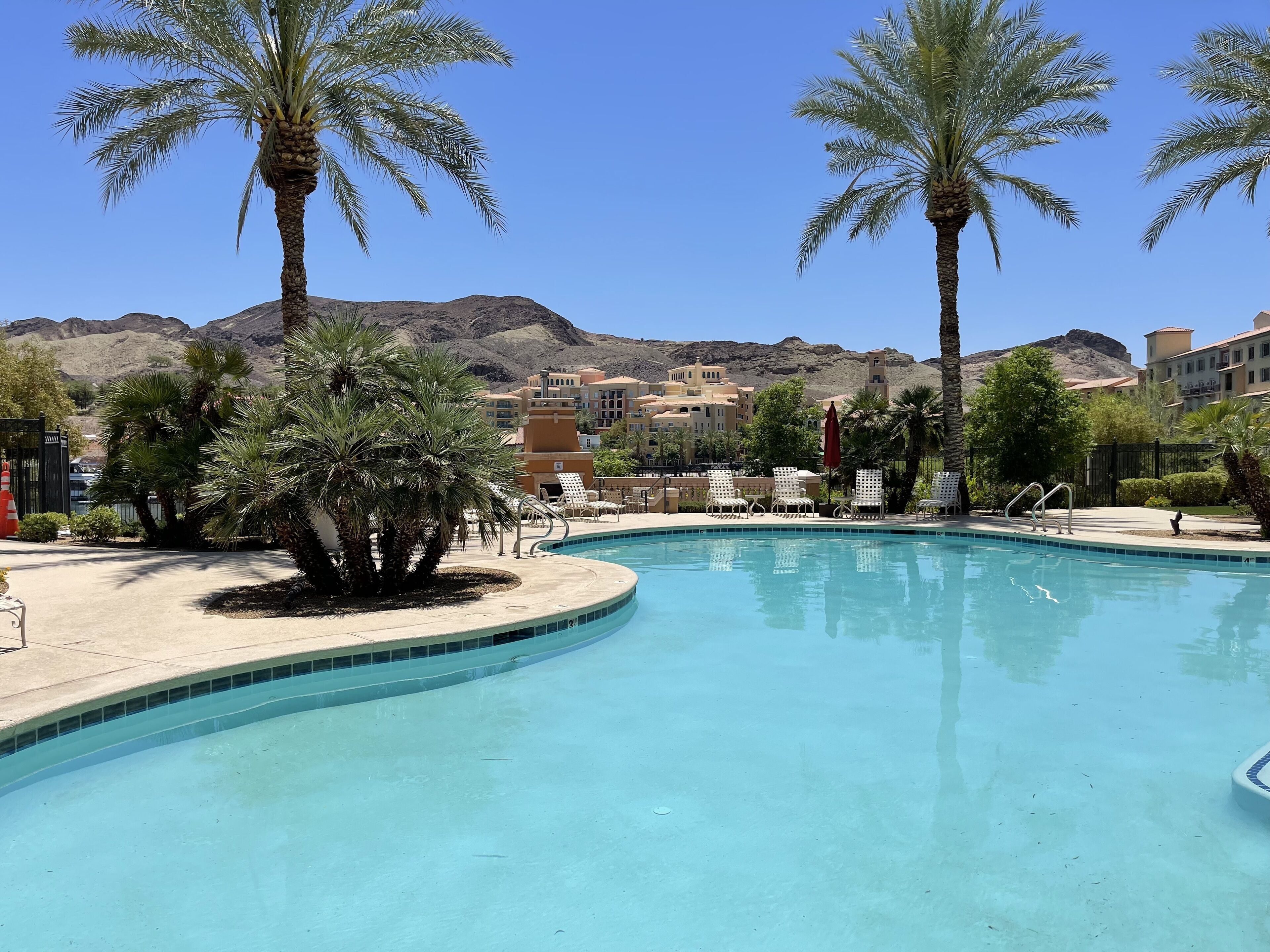 A swimming pool with palm trees, lounge chairs, and a mountain backdrop.