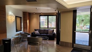 Eine moderne Lobby mit einer Couch, Sesseln, einem Glastisch, einem Mülleimer und einer Tür zum Ausgang.