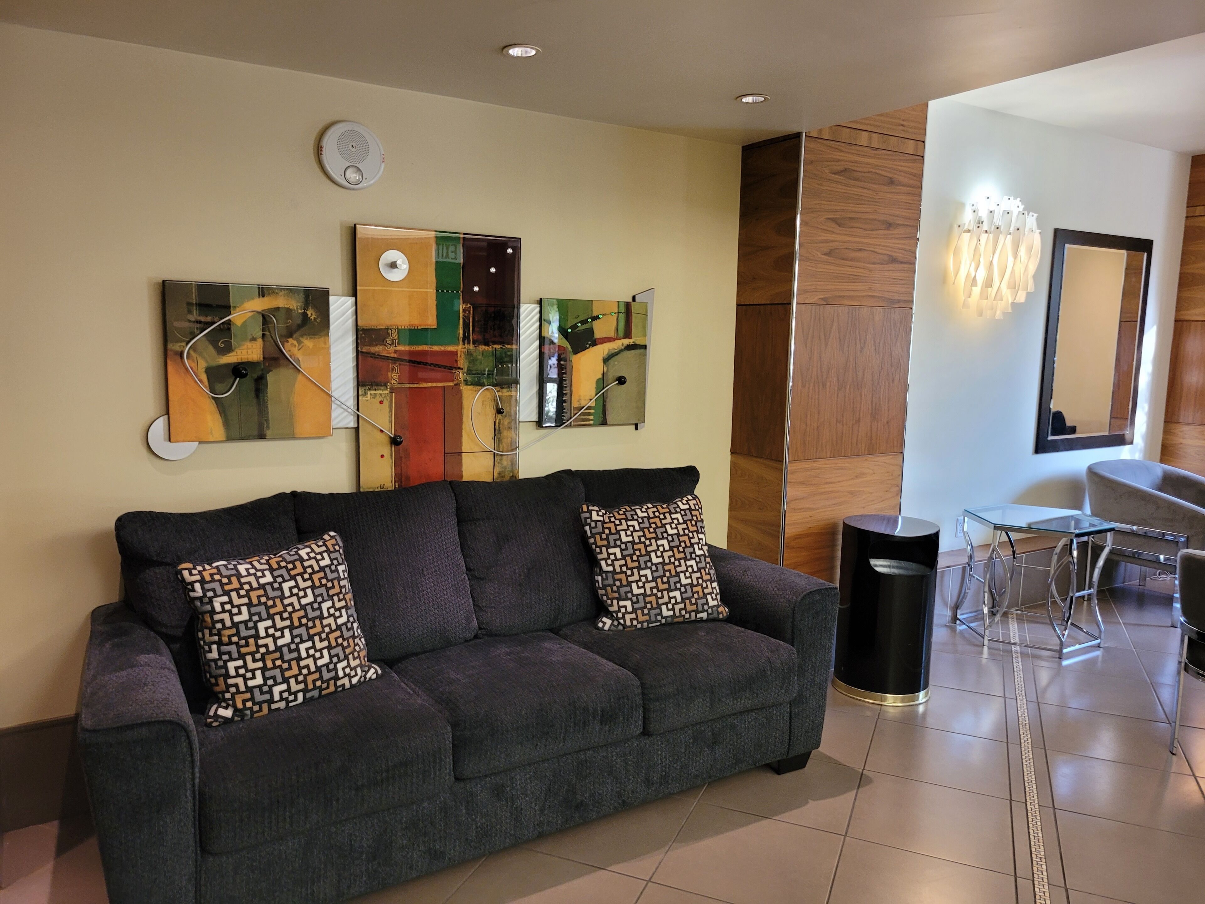 Una sala de estar moderna con un sofá gris, arte abstracto en la pared, un panel de pared de madera, una mesa de comedor de vidrio y un cubo de basura negro.