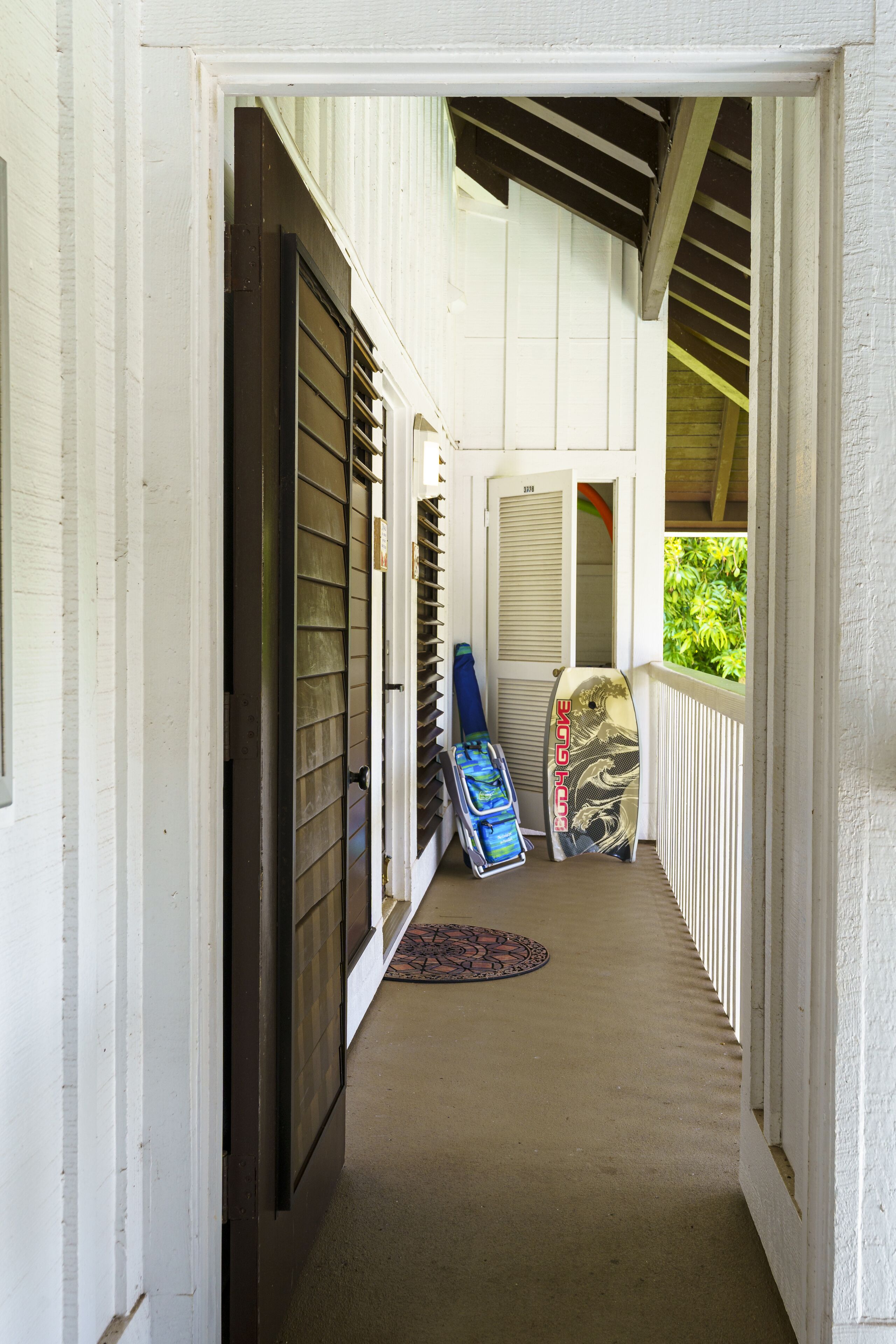 A covered porch with a concrete floor, a door with a metal gate, and a surfboard leaning against the wall.