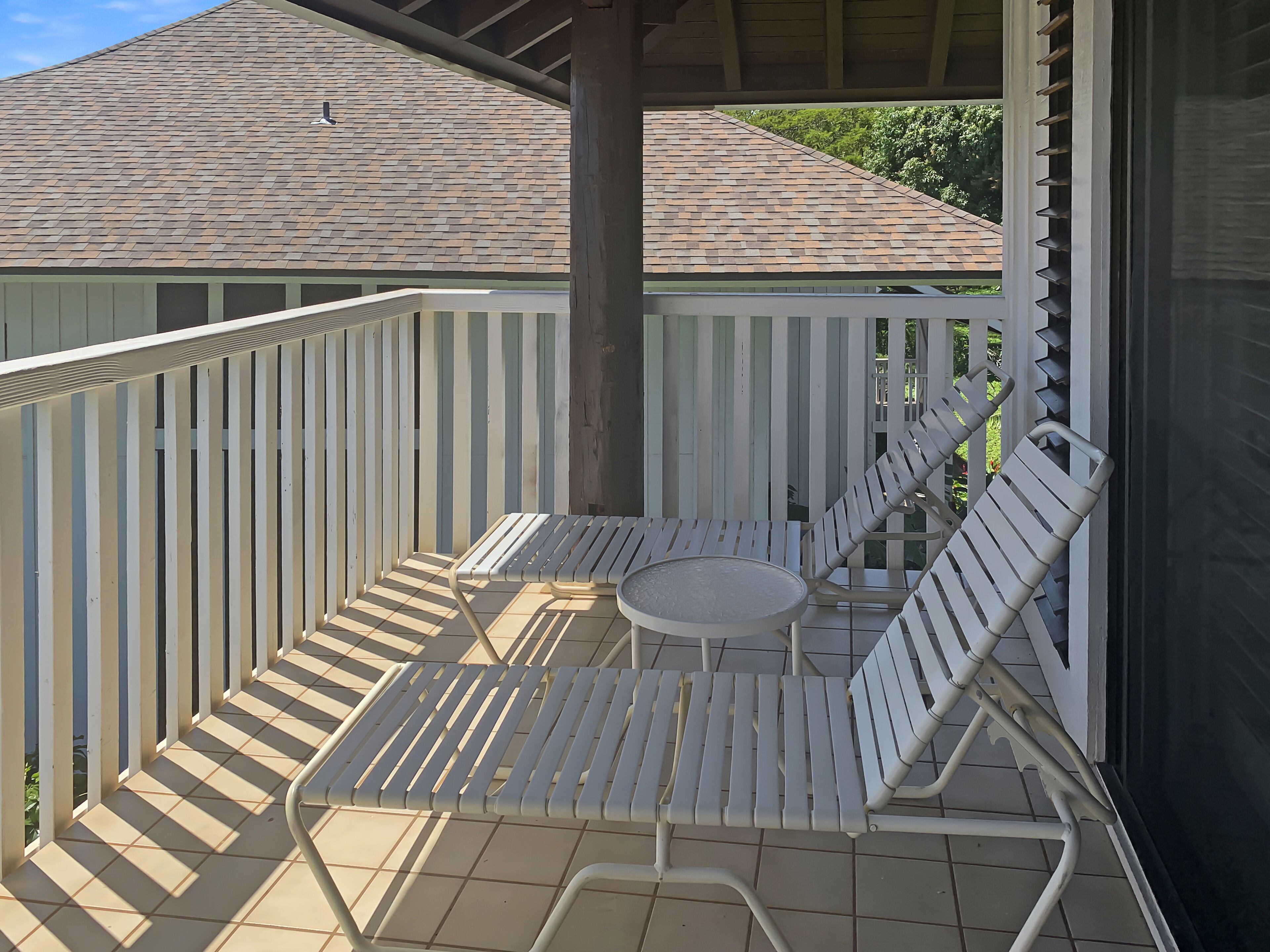 Un balcon abrité, avec des chaises en métal blanc et une petite table ronde.