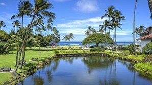 A serene resort setting with a calm pond, lush greenery, and a view of the ocean. - Poipu Condo!  Newly updated - Sleeps 5 - 5 minute walk to the beach! (Koloa)