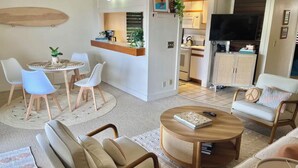 A modern living room with a round coffee table, beige sofas, and a dining area with a round table and chairs. - Poipu Condo!  Newly updated - Sleeps 5 - 5 minute walk to the beach! (Koloa)