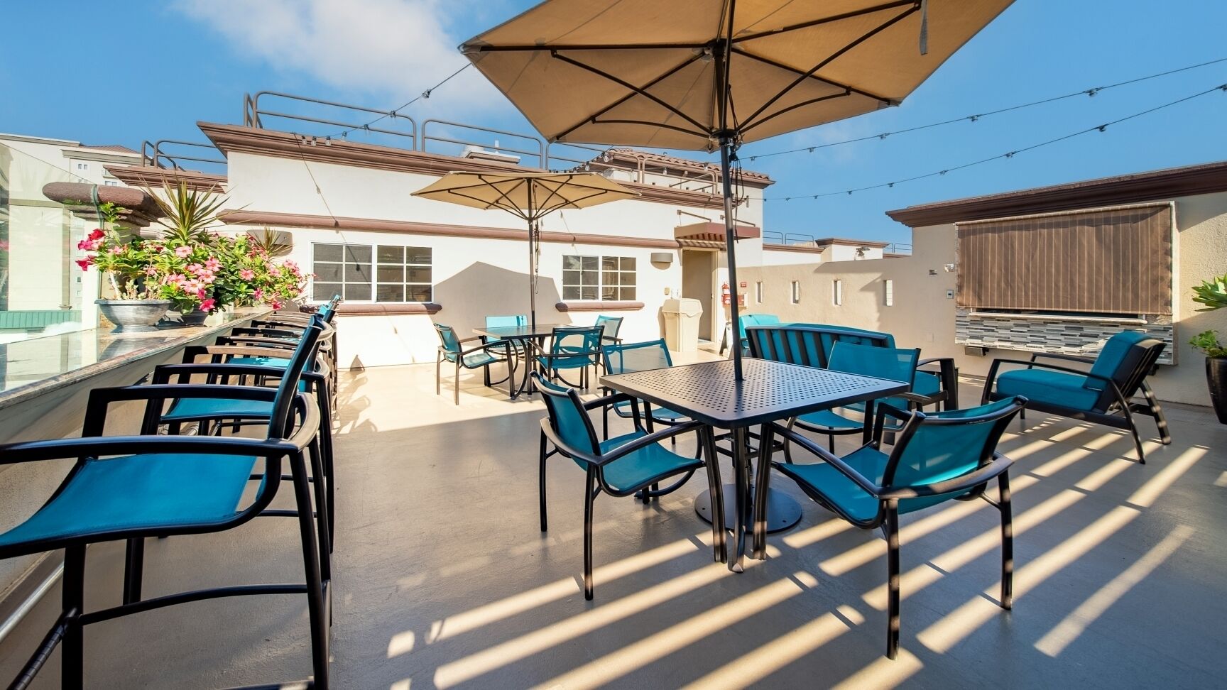 Une terrasse extérieure avec des tables et des chaises, un grand parasol et un bâtiment en arrière-plan.