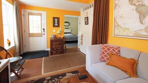 Habitación de hotel con sofá, mesa de comedor, silla, cama, mapa en la pared y ventana con cortinas.