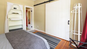 Un dormitorio con cama, armario, tendedero y puerta que da a otra habitación.