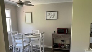 A dining area with a white table and chairs, a ceiling fan, a microwave, and a small cabinet with kitchen appliances. - Adventure Acres- Suite B8  (Holly)