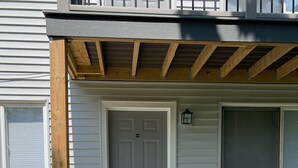 A residential building with a grey door, a small porch with a wooden beam, and a window with a screen. - Adventure Acres- Suite B8  (Holly)