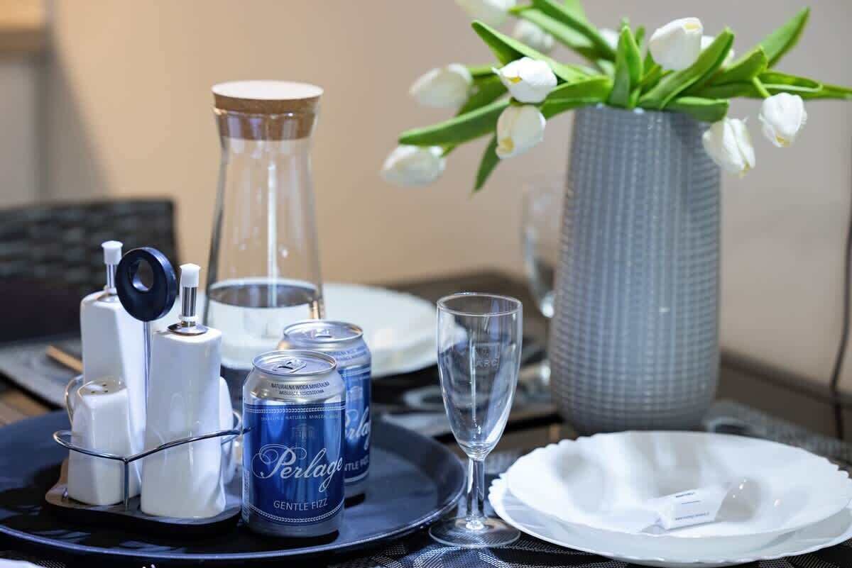 Ein Tisch gedeckt mit einer Perlage-Bierdose, einem Glas, Salzhändlern und einer Vase mit weißen Blumen.