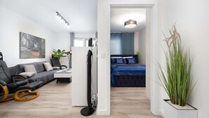 Una sala moderna con un sofá, una mesa de centro y una televisión. En la habitación contigua hay una cama con cabecera azul.