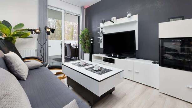 Una sala de estar moderna con sofá, mesa de centro, televisor y área de cocina.