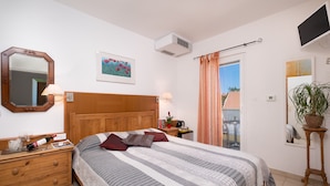 Un dormitorio con cabecera de madera, una cama grande con ropa de cama a rayas, una mesita de noche con lámpara, un espejo y una planta en maceta.