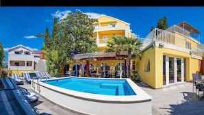 Un hotel con piscina, zona de estar exterior y un edificio amarillo con balcones.