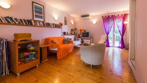 Una sala de estar acogedora con piso de madera, una estantería, un televisor y un sofá.