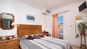 Un dormitorio con cabecera de madera, una cama grande con ropa de cama a rayas, una mesita de noche con lámpara, un espejo y una planta en maceta.