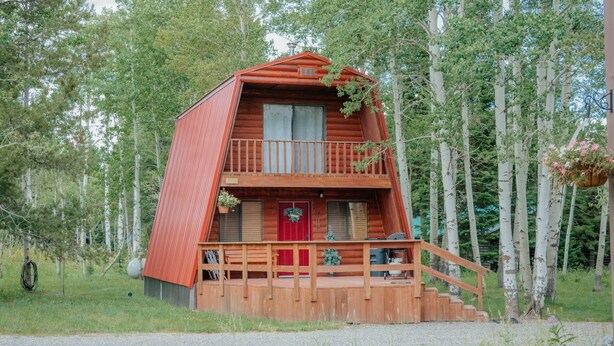 A wooden cabin with a red door, a balcony, and a staircase leading to the entrance. - Aspen Ridge Cabin WIFI, 2bed+1Bath, 20mins to Yellowstone (Island Park)