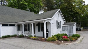 A white two-story house with a porch, a small attached garage, and a garden with various plants and flowers.