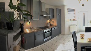 A modern kitchen with grey cabinets, a dining table with plates, and a sofa in the living area.
