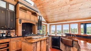 A spacious kitchen with wooden cabinets, a large island, and a view of the outdoors through large windows. - Lake View Chalet! Game Room! Hot Tub! (Silverpoint)