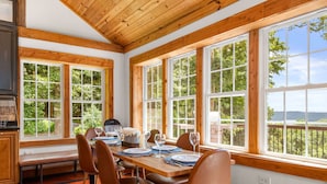 A dining area with a wooden table set for four, large windows, and a view of greenery. - Lake View Chalet! Game Room! Hot Tub! (Silverpoint)