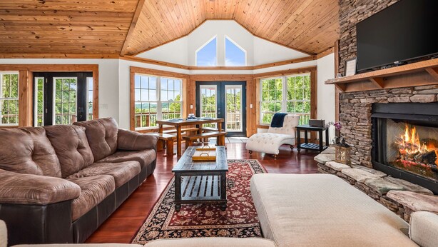 A spacious living room with a stone fireplace, wooden ceiling, and large windows. - Lake View Chalet! Game Room! Hot Tub! (Silverpoint)