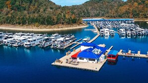 A marina with numerous boats docked, a small dock with a blue roof, and a forested hillside in the background. - Lake View Chalet! Game Room! Hot Tub! (Silverpoint)