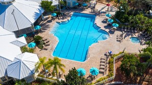 Vue aérienne d’un complexe hôtelier doté d’une grande piscine centrale, de plusieurs petites piscines et d’espaces de détente en plein air agrémentés de parasols.
