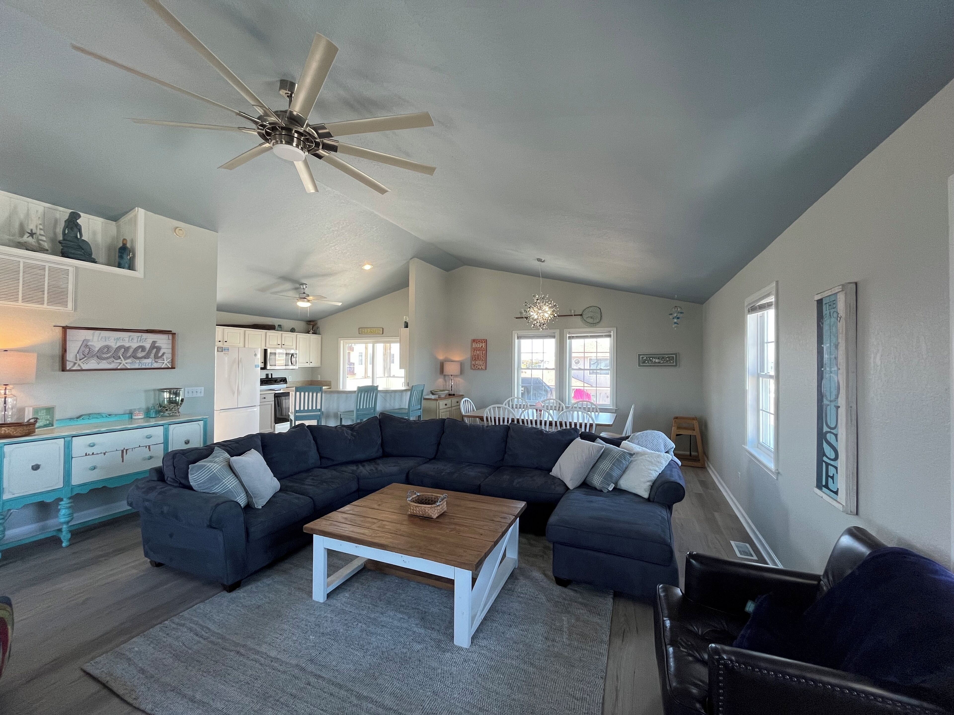 A spacious living room with a dark sectional sofa, a wooden coffee table, and a ceiling fan.