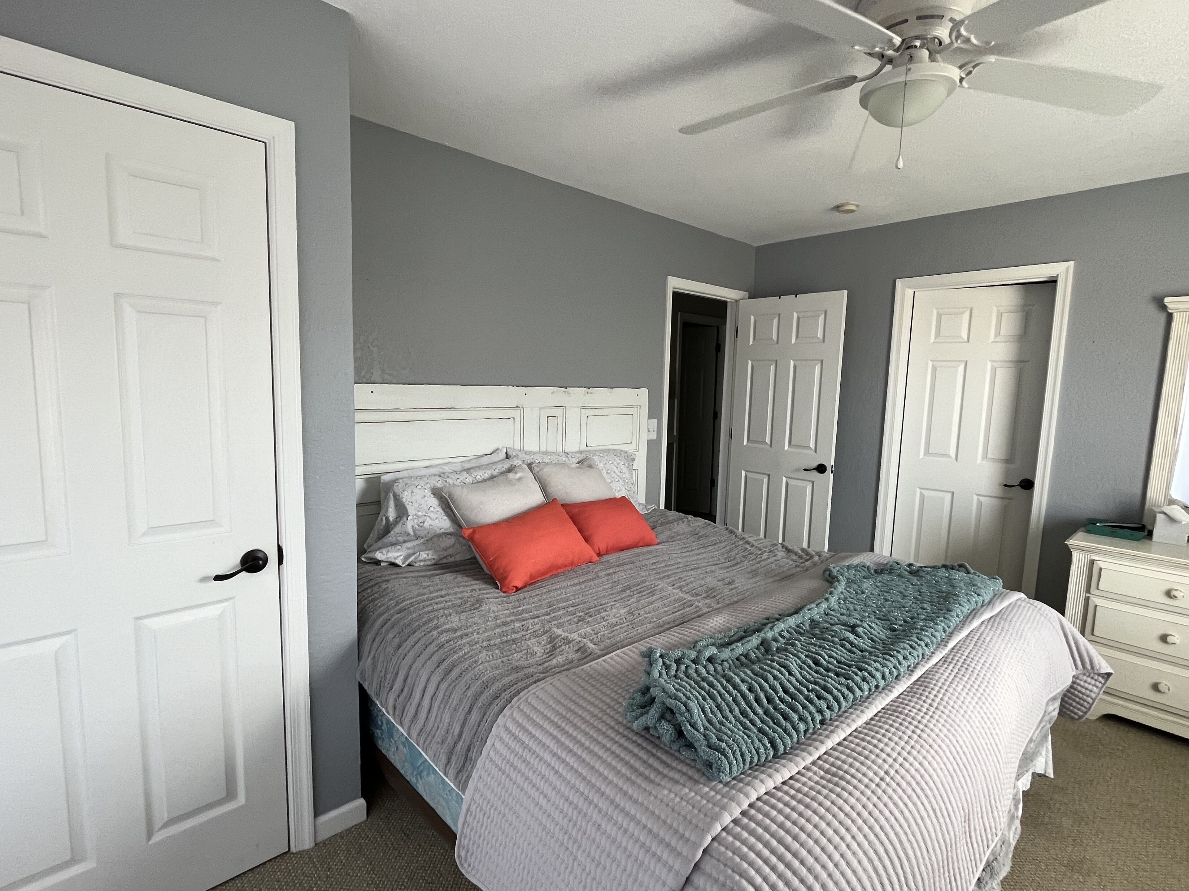 Une chambre à coucher avec un lit, un ventilateur de plafond et des portes blanches.
