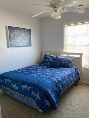 Ein Schlafzimmer mit einem Bett, einem Deckenventilator, einem Fenster mit Jalousien und einem Wandbild.