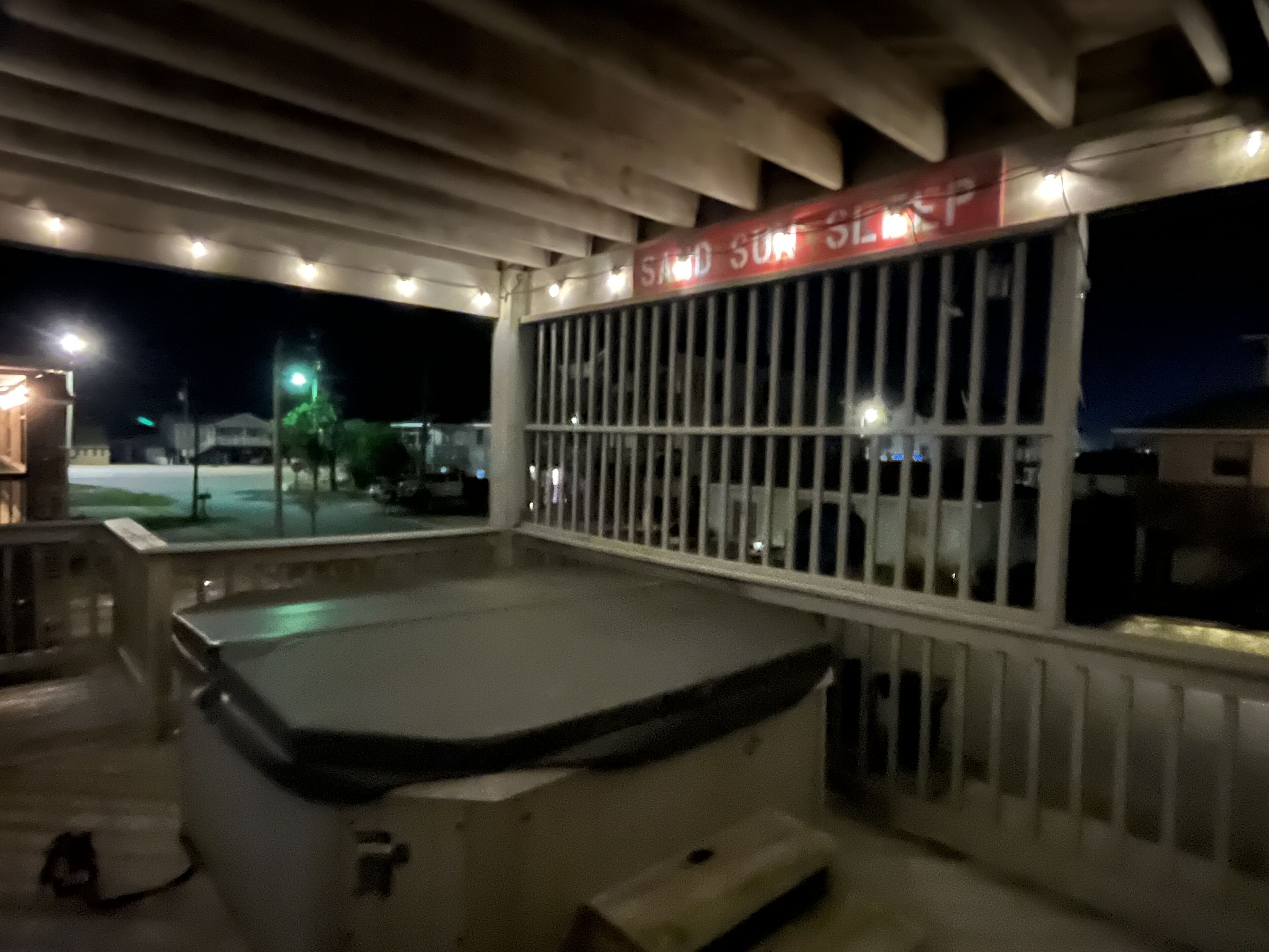 A covered outdoor area with a pool, a railing, and a sign that reads "SAND SUN SLEEP".