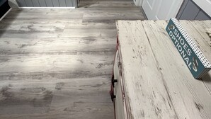 Un pasillo con suelo de madera, paredes blancas y puertas a ambos lados.