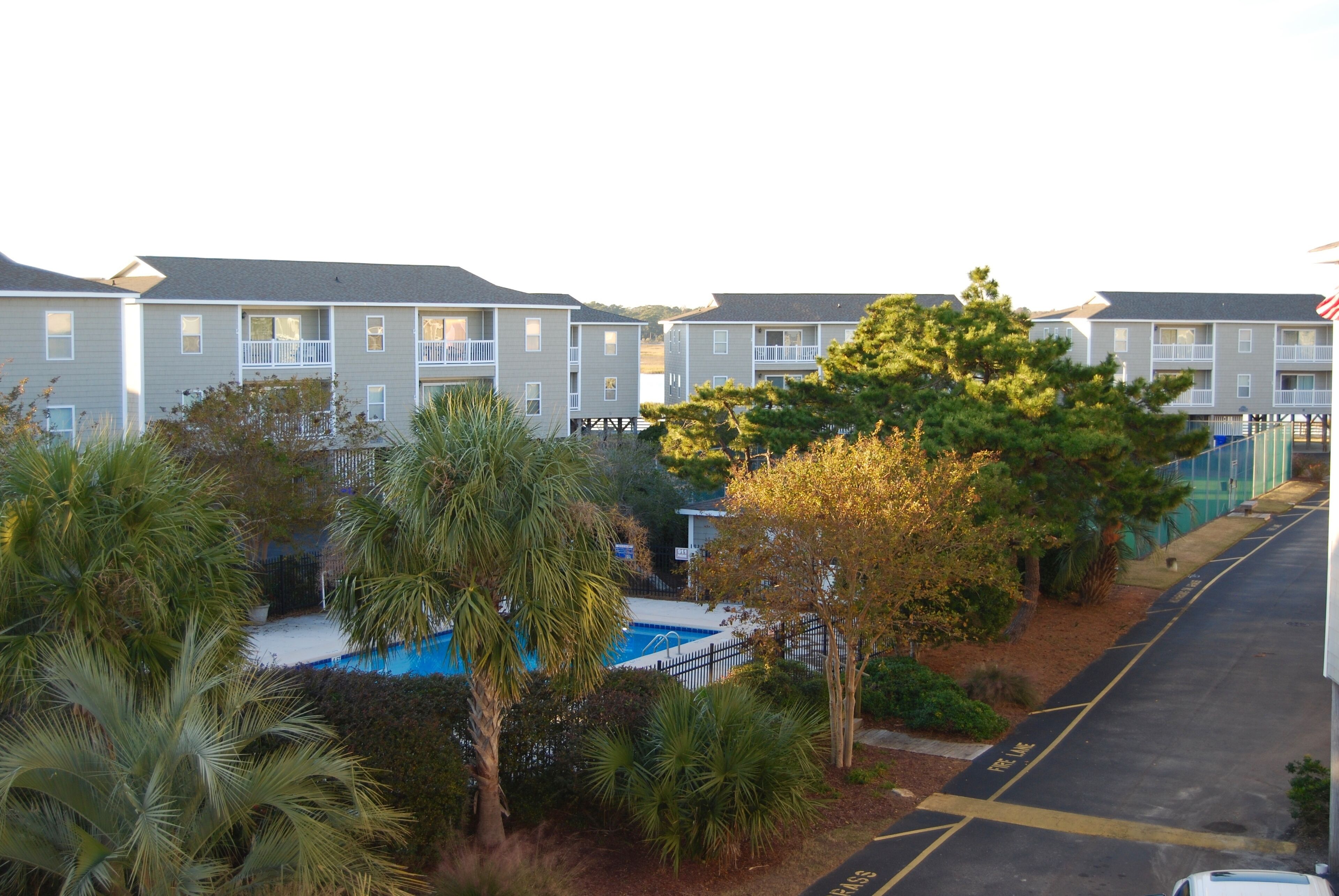 A multi-story residential building with balconies, a swimming pool, and a parking area.