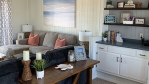 Un salon chaleureux avec un canapé, une table basse en bois et un coin cuisine doté de meubles et d’étagères blancs.