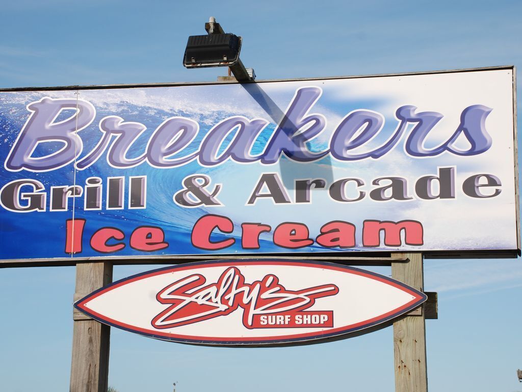 A sign for a restaurant named 'Breakers Grill & Arcade Ice Cream' with a surf shop logo below.