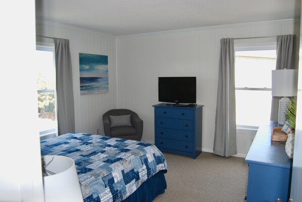 A bedroom with a bed, a chair, a dresser, a television, and a window. - Beautiful OIB Condo- 1 Min. Walk to Beach; includes Pools, Tennis Courts, Extras (Ocean Isle Beach)