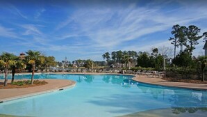 A large, clear swimming pool with lounge chairs and palm trees, surrounded by a landscaped area. - Hampton Hall Golf Cottage (Bluffton)