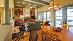 A spacious living room with a fireplace, a dining area, and a large window with a view. - Hampton Hall Golf Cottage (Bluffton)