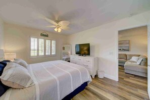 Une chambre à coucher avec un lit, une télévision, une commode, un ventilateur de plafond et une fenêtre.