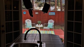 Une cuisine équipée d’un évier et de luminaires suspendus, une clôture rouge et un espace extérieur aménagé avec des chaises et une table.