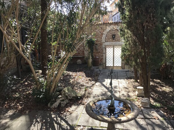 A courtyard with a fountain, stone pathway, and a building with a tiled entrance. - Studio With Private Garden (Venezia)