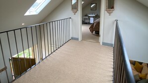 A high-ceilinged attic bedroom with skylights, a staircase, and a view into the bathroom. - Rectory Farm Barn (Grantham)