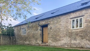 A stone building with a wooden door, two windows, and a sloped roof. - Rectory Farm Barn (Grantham)