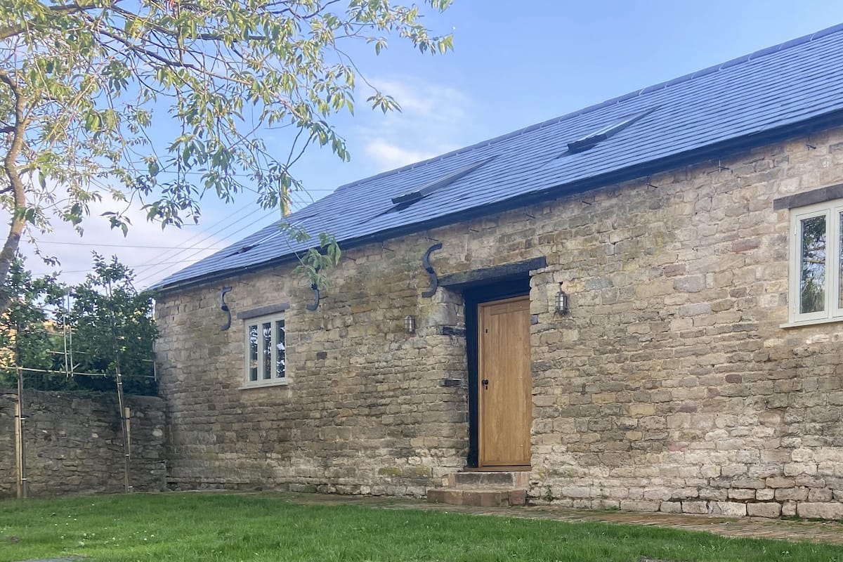 Un edificio de piedra con puerta de madera, dos ventanas y techo inclinado.