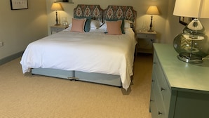 A neatly made bed with a patterned headboard, two bedside tables with lamps, and a dresser with a mirror. - Rectory Farm Barn (Grantham)