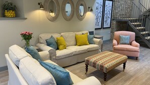 A living room with a beige sofa, a patterned ottoman, and a pink armchair. There are three wall-mounted mirrors and a potted plant with yellow lemons. - Rectory Farm Barn (Grantham)