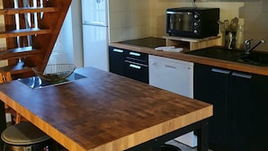 A kitchen with a wooden table, stools, a microwave, a dishwasher, and cabinets. - Appartement Authentique Dans le Centre de Caen (Caen)
